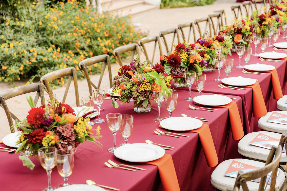 Long dinner table with burgundy and orange linens and colorful flowers